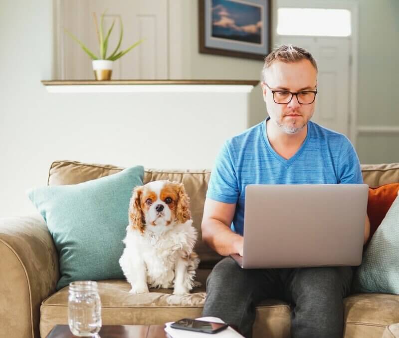 pets positive mental health outcomes business man working from home on laptop computer telecommuting on couch working remote with dog friendly drug rehab