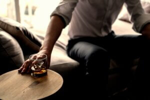 sign of mental health disorder man reaching for whiskey on ice alcoholic cocktail liquor drink while sitting on a comfy lounge chair