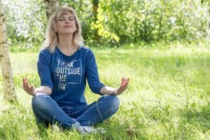 young woman being mindful sits on the grass near a tree and meditates female woman lifestyle exercise health tips on minfulness training