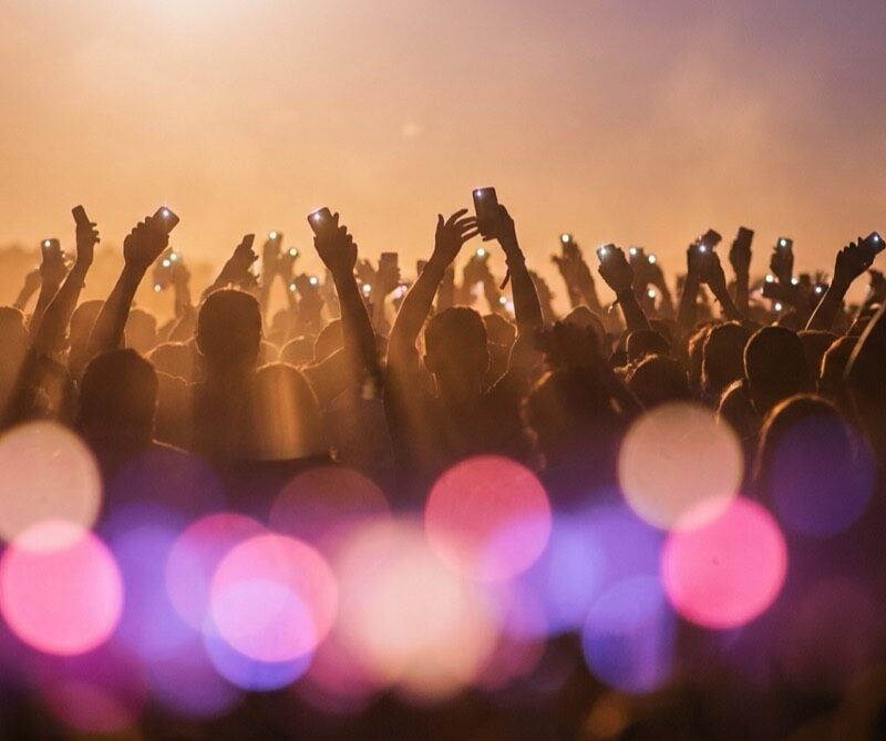Concert crowd silhouettes raising phone lights under pink and purple stage lighting at a pop show