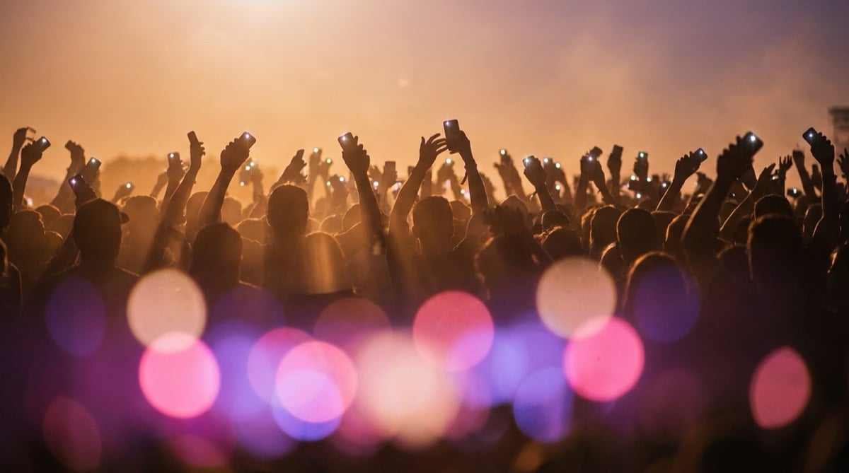 Concert crowd silhouettes raising phone lights under pink and purple stage lighting at a pop show