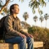 Young adult easing anxiety with a grounding technique, breathing calmly on a park bench in morning light